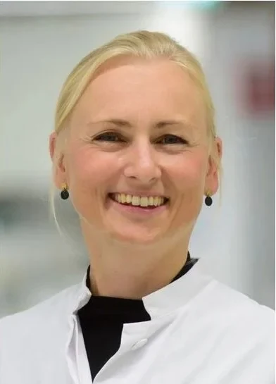 Eine Wissenschaftlerin und ein Wissenschaftler arbeiten hinter einer Glasfassade und mischen Chemikalien mit Großgeräten.